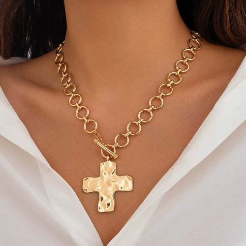 A gold-tone chain necklace with a hammered cross pendant, worn by a model in a white blouse.